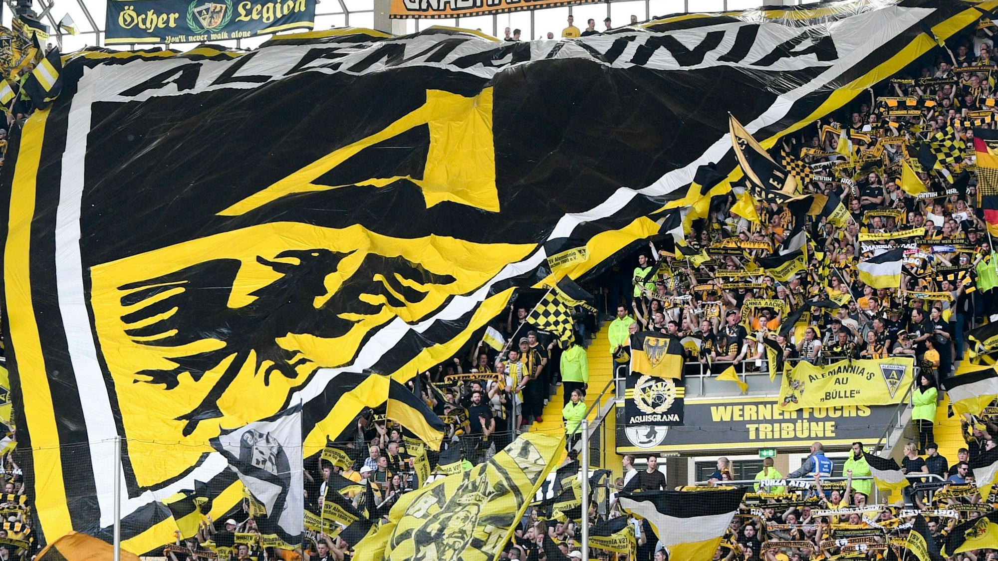 Die Aachener Fankurve hält einen großen Banner mit dem Alemannia-Wappen hoch.