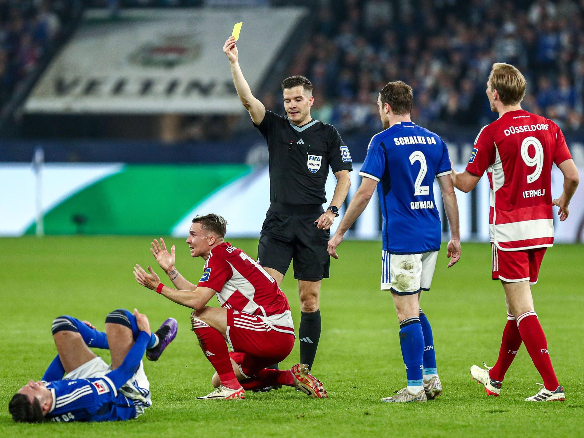 Fortuna Düsseldorfs Felix Klaus kniet am Boden, Schiedsrichter Harm Osmers zeigt ihm die Gelbe Karte.