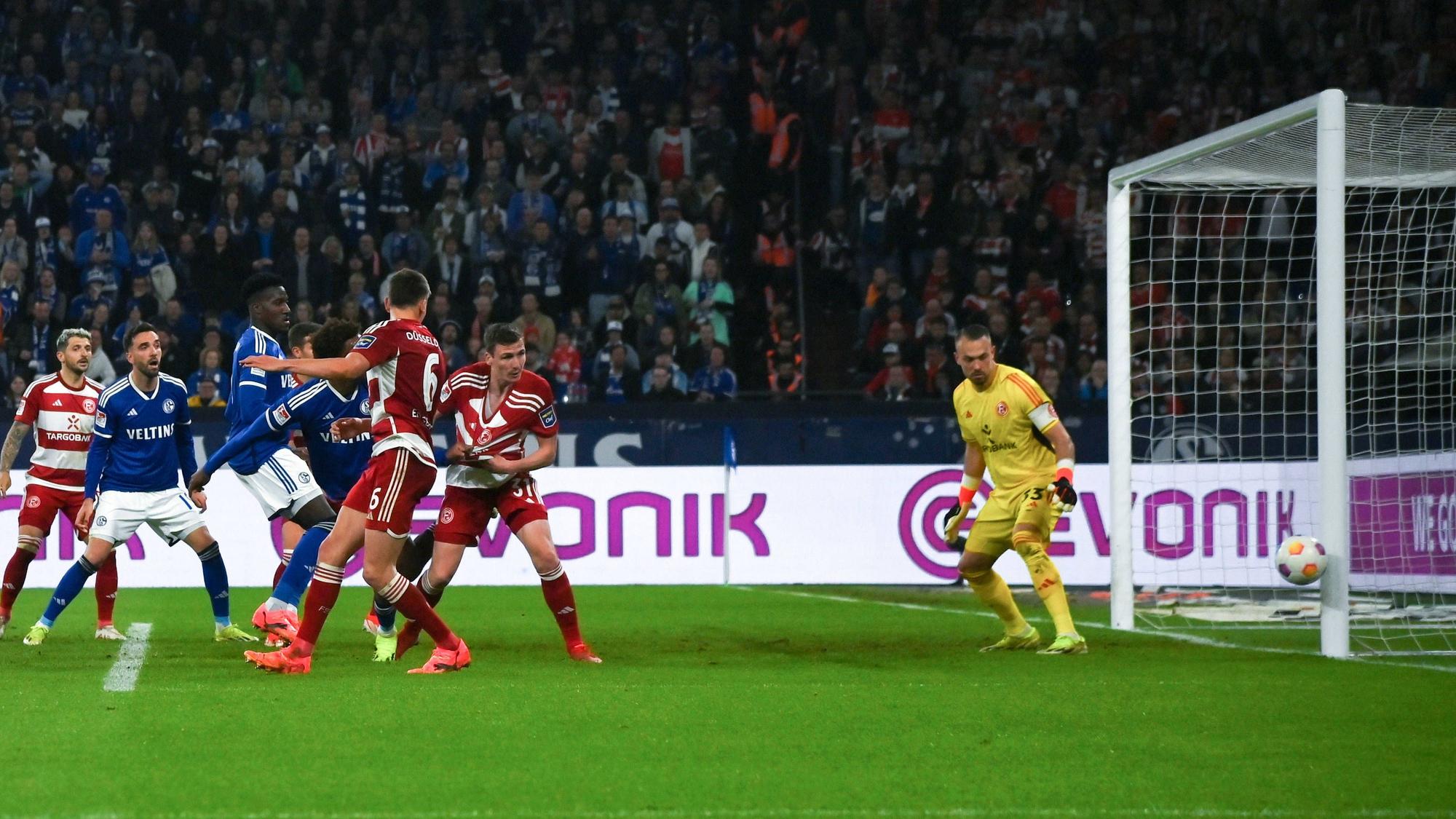 Fortuna Düsseldorf und Schalke 04 Spieler schauen auf den Ball, der den Pfosten vom Tor trifft.