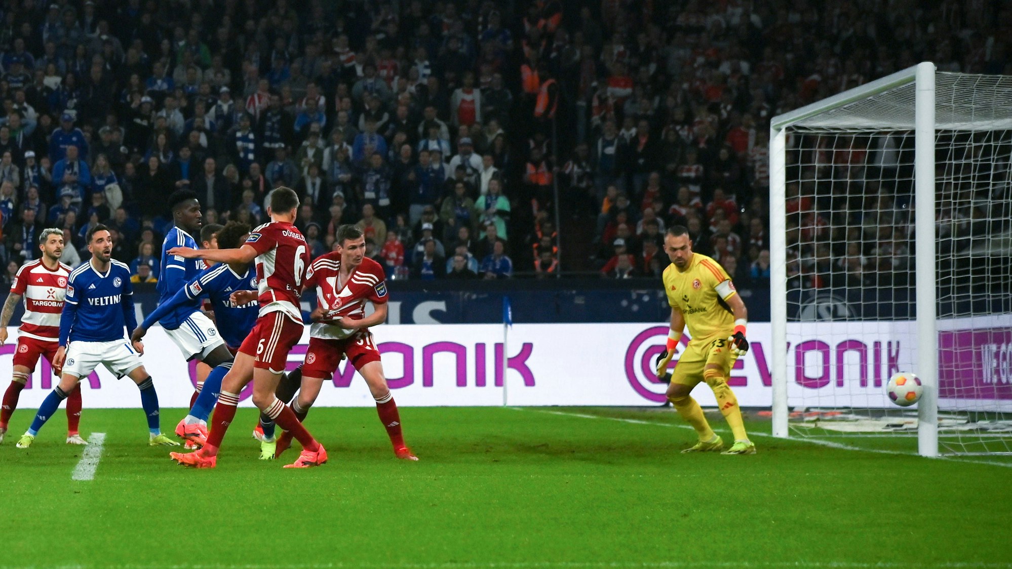 Fortuna Düsseldorf und Schalke 04 Spieler schauen auf den Ball, der den Pfosten vom Tor trifft.