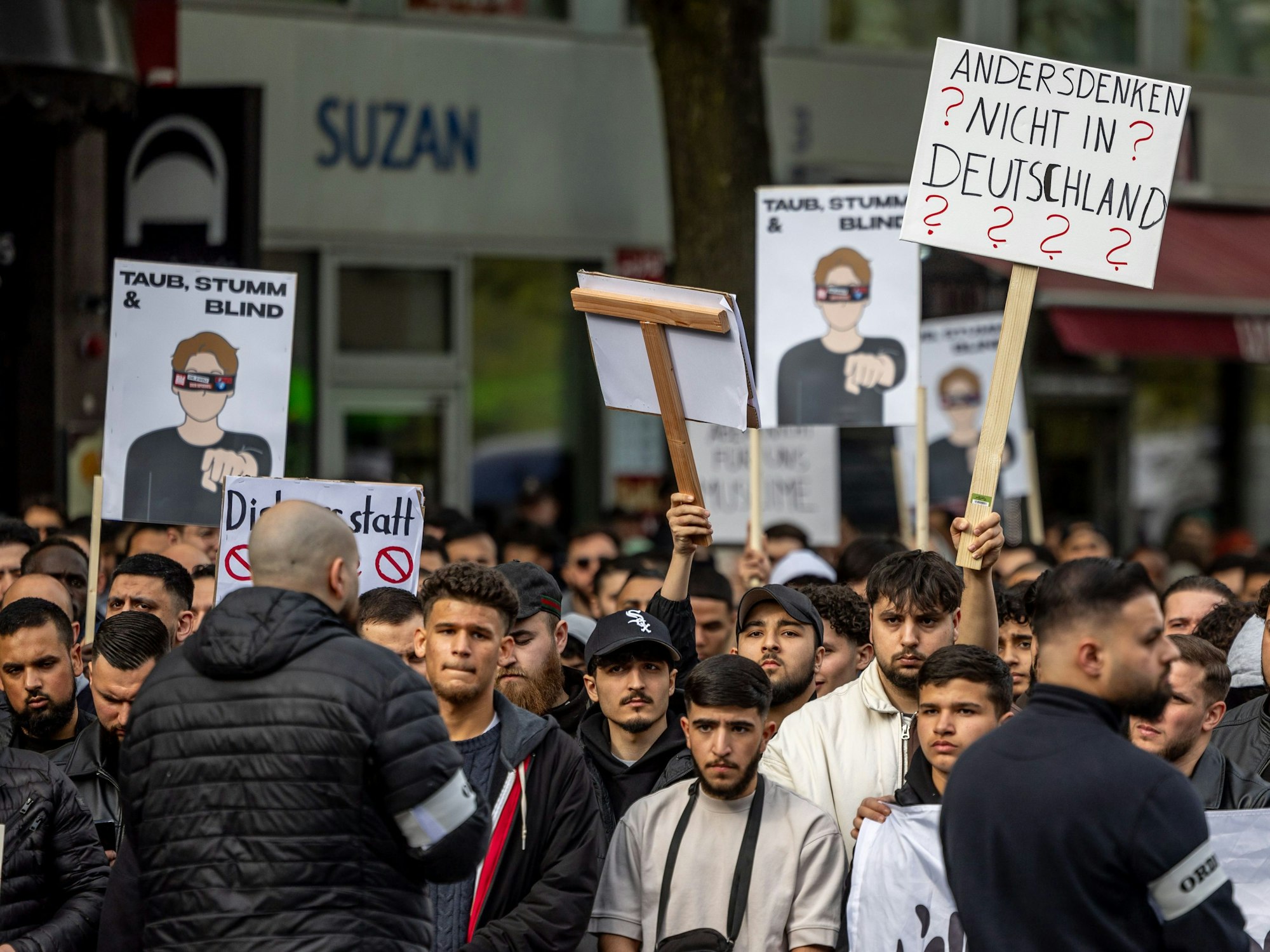Teilnehmende einer Islamisten-Demo in Hamburg halten am Samstag (27. April 2024) ein Plakat mit der Aufschrift „Andersdenken? Nicht in Deutschland“ in die Höhe.