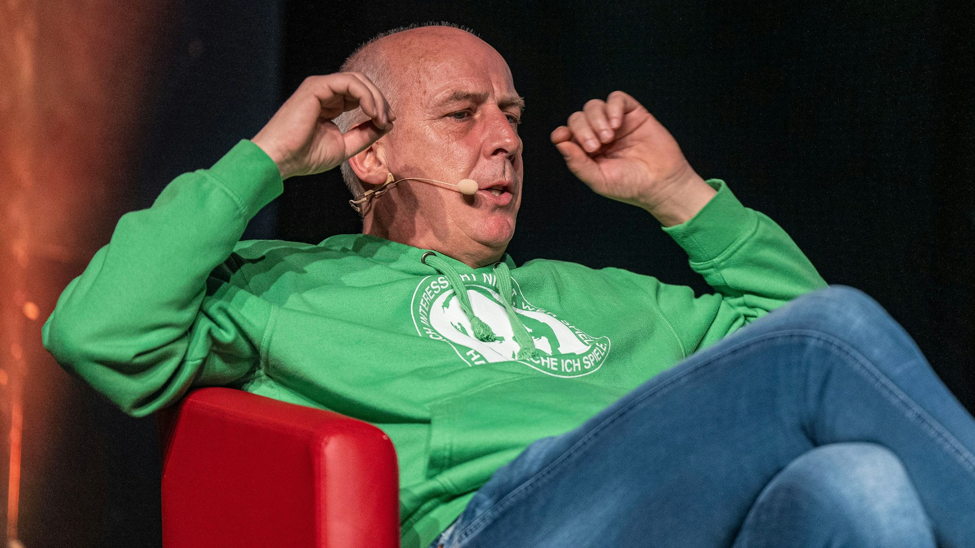 Mario Basler sitzt bei einer Veranstaltung des „Doppelpass on Tour“ auf der Bühne.