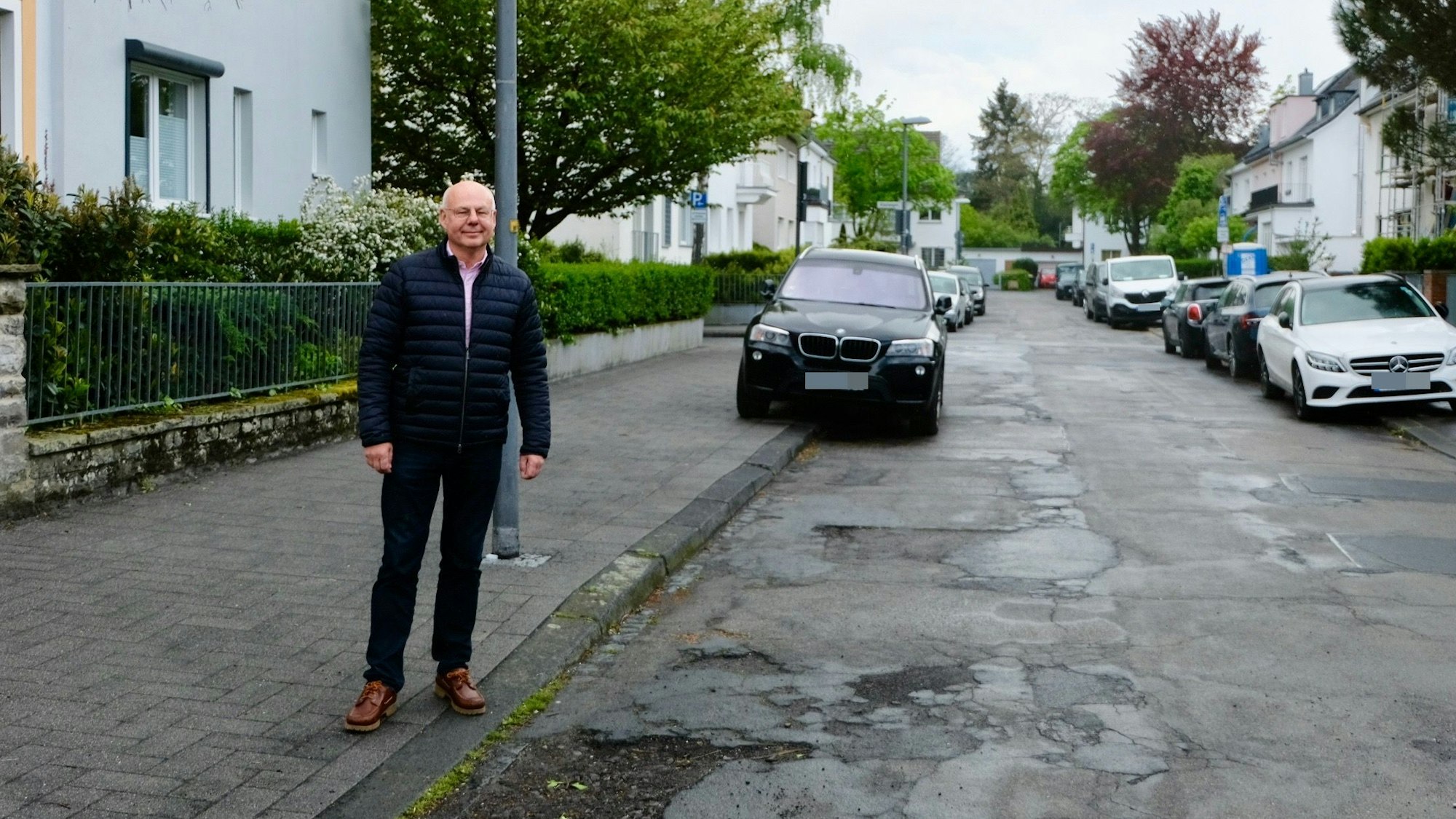 Joachim Hüttl auf dem frisch gepflasterten Gehweg der Von-Lauff-Straße neben der löchrigen Fahrbahn.