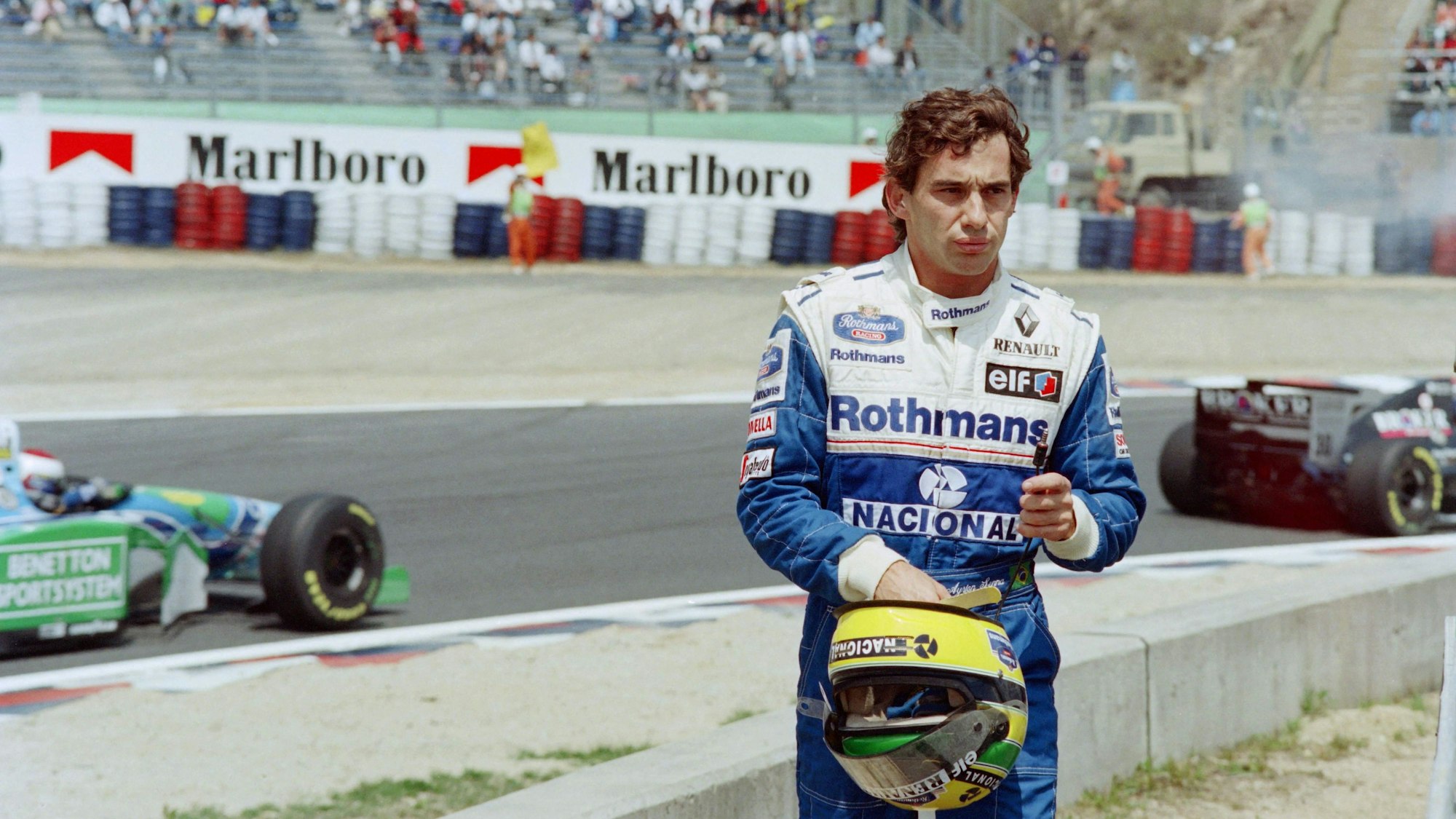 Ayrton Senna steht nach seinem Ausscheiden aus dem Pacific Grand Prix der Formel 1 der Rennstrecke, im Hintergrund fahren die anderen Autos.