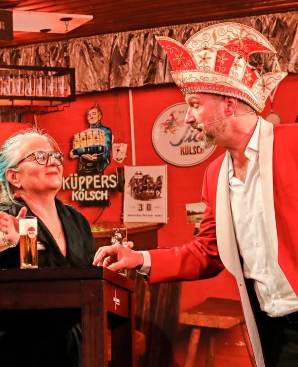 Volker Weininger in seinem Outfit als Sitzungspräsident auf der Bühne. Eine Frau bringt ihm dabei ein neues Kölsch.