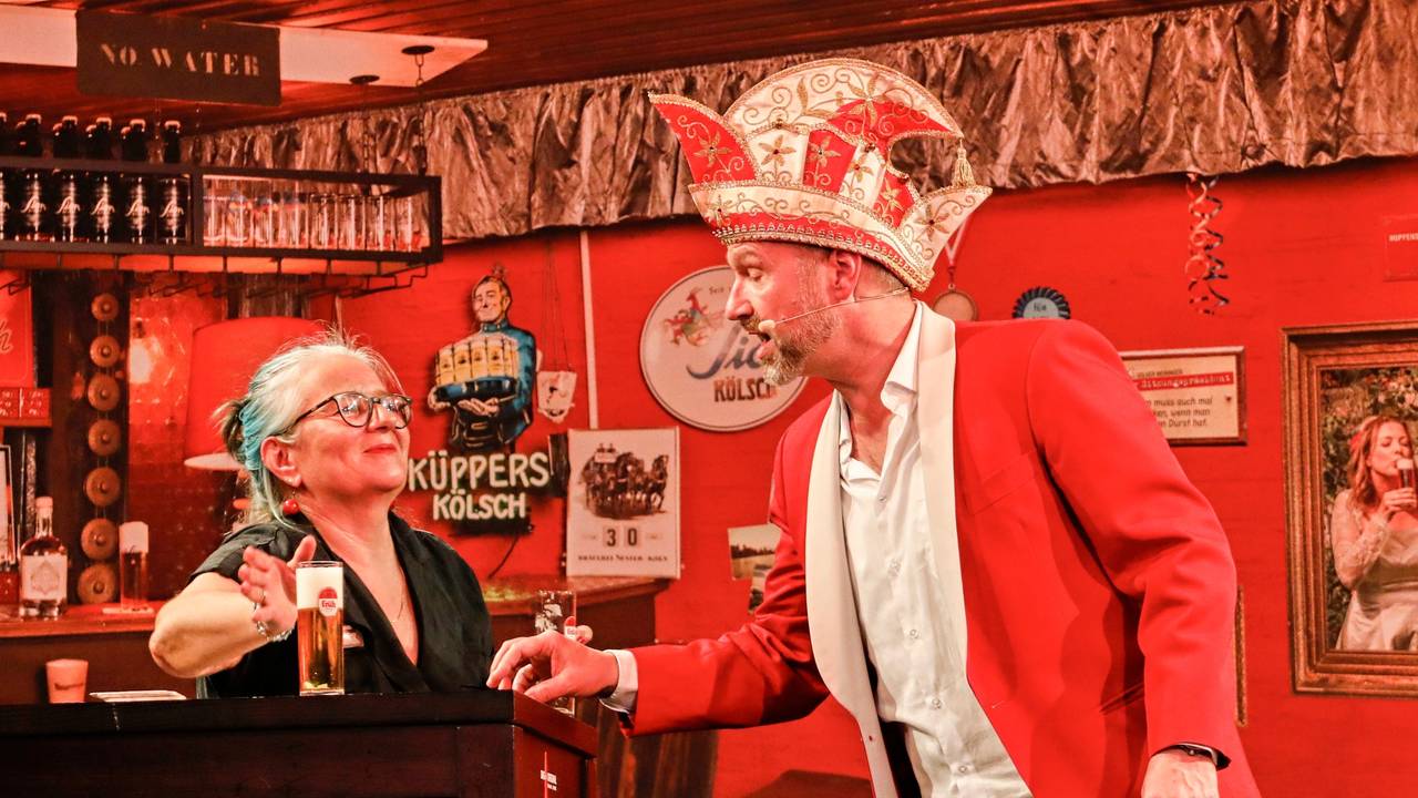 Volker Weininger in seinem Outfit als Sitzungspräsident auf der Bühne. Eine Frau bringt ihm dabei ein neues Kölsch.