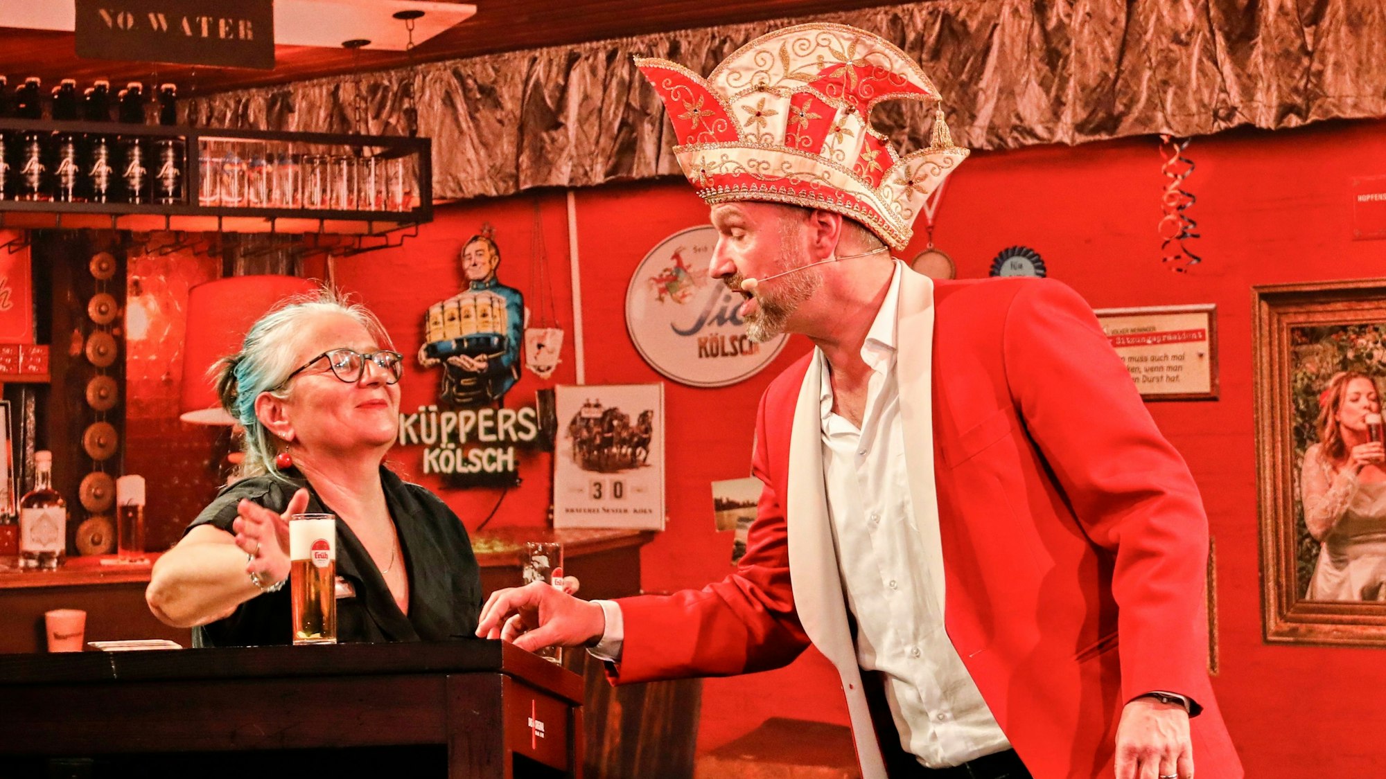 Volker Weininger in seinem Outfit als Sitzungspräsident auf der Bühne. Eine Frau bringt ihm dabei ein neues Kölsch.