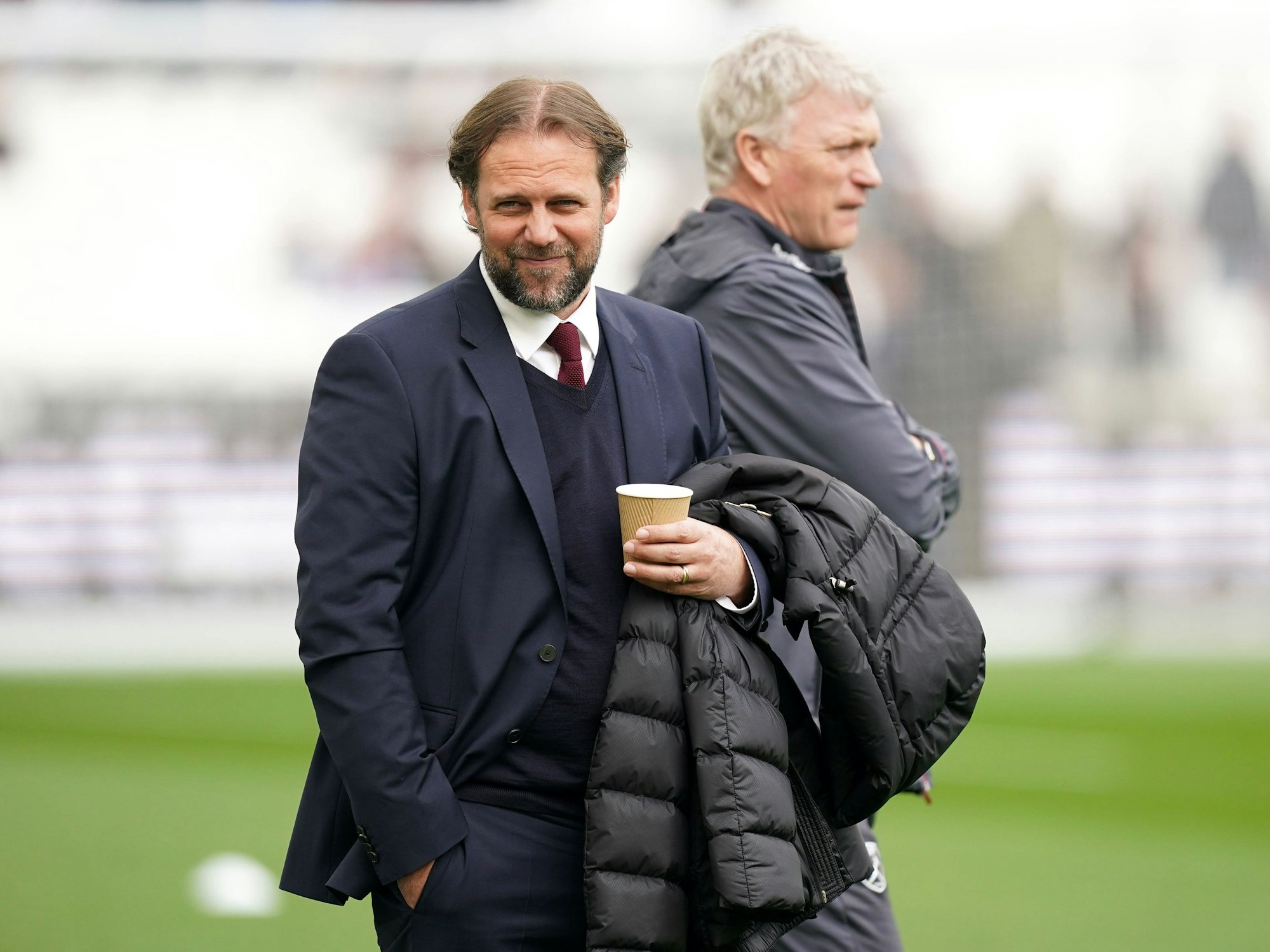 Tim Steidten mit Kaffeebecher in der Hand, im Hintergrund steht David Moyes.
