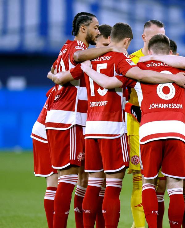 Das Team von Fortuna Düsseldorf steht vor dem Anpfiff des Auswärtsspiels beim FC Schalke 04 Arm in Arm am Mittelkreis zusammen.
