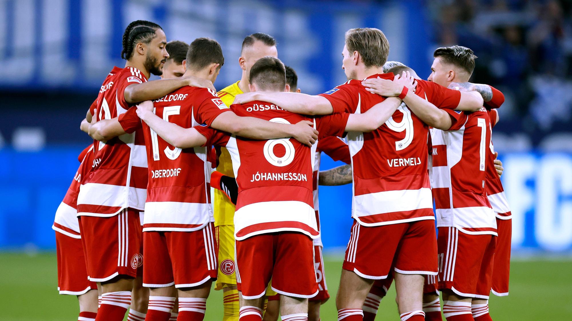 Das Team von Fortuna Düsseldorf steht vor dem Anpfiff des Auswärtsspiels beim FC Schalke 04 Arm in Arm am Mittelkreis zusammen.