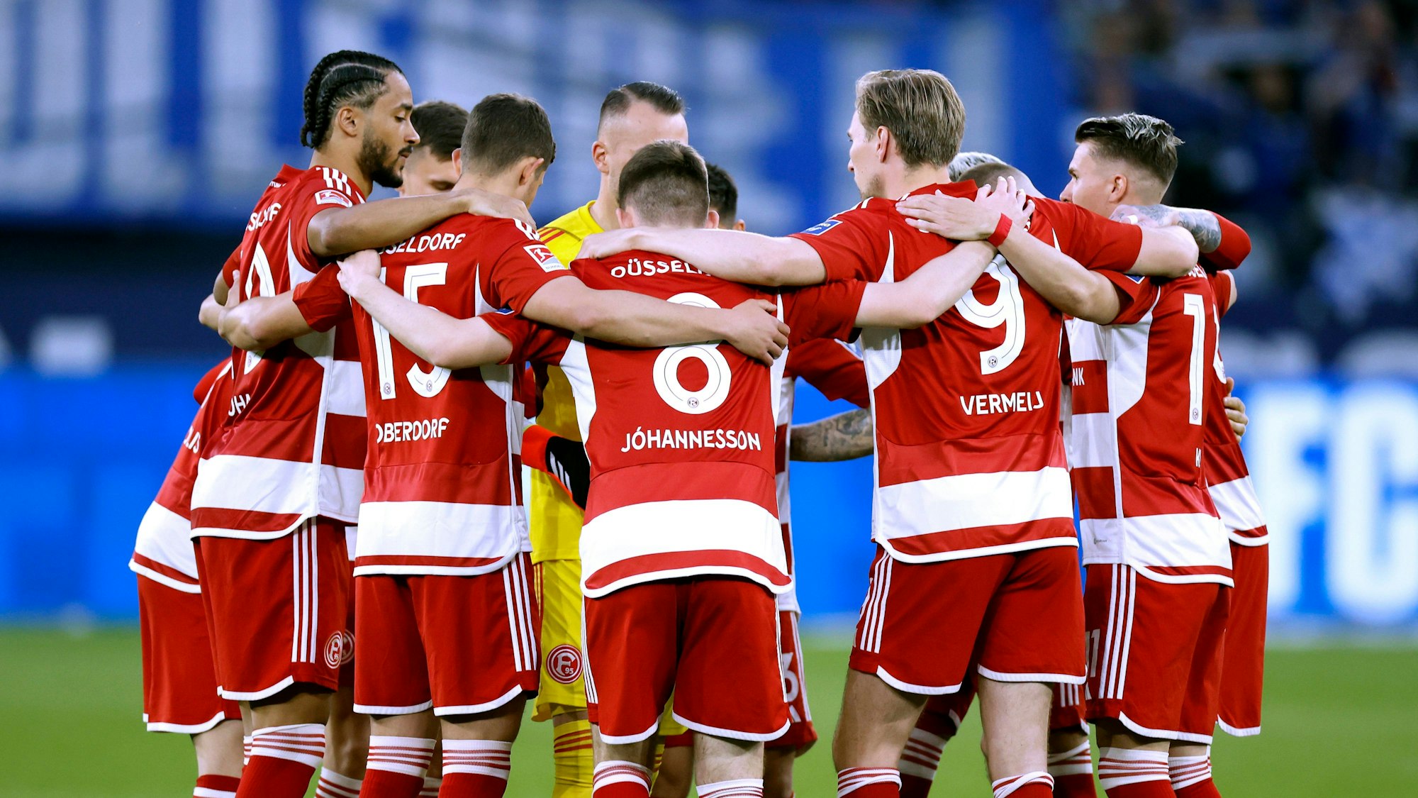 Das Team von Fortuna Düsseldorf steht vor dem Anpfiff des Auswärtsspiels beim FC Schalke 04 Arm in Arm am Mittelkreis zusammen.