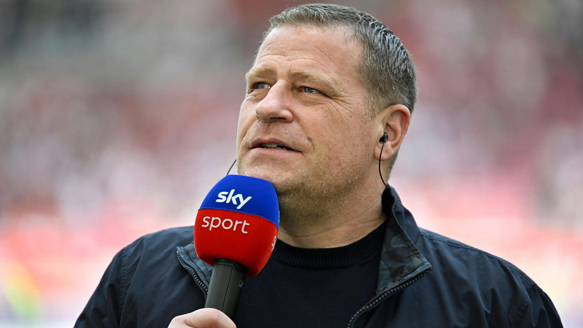 Max Eberl steht mit Mikrofon am Spielfeldrand.