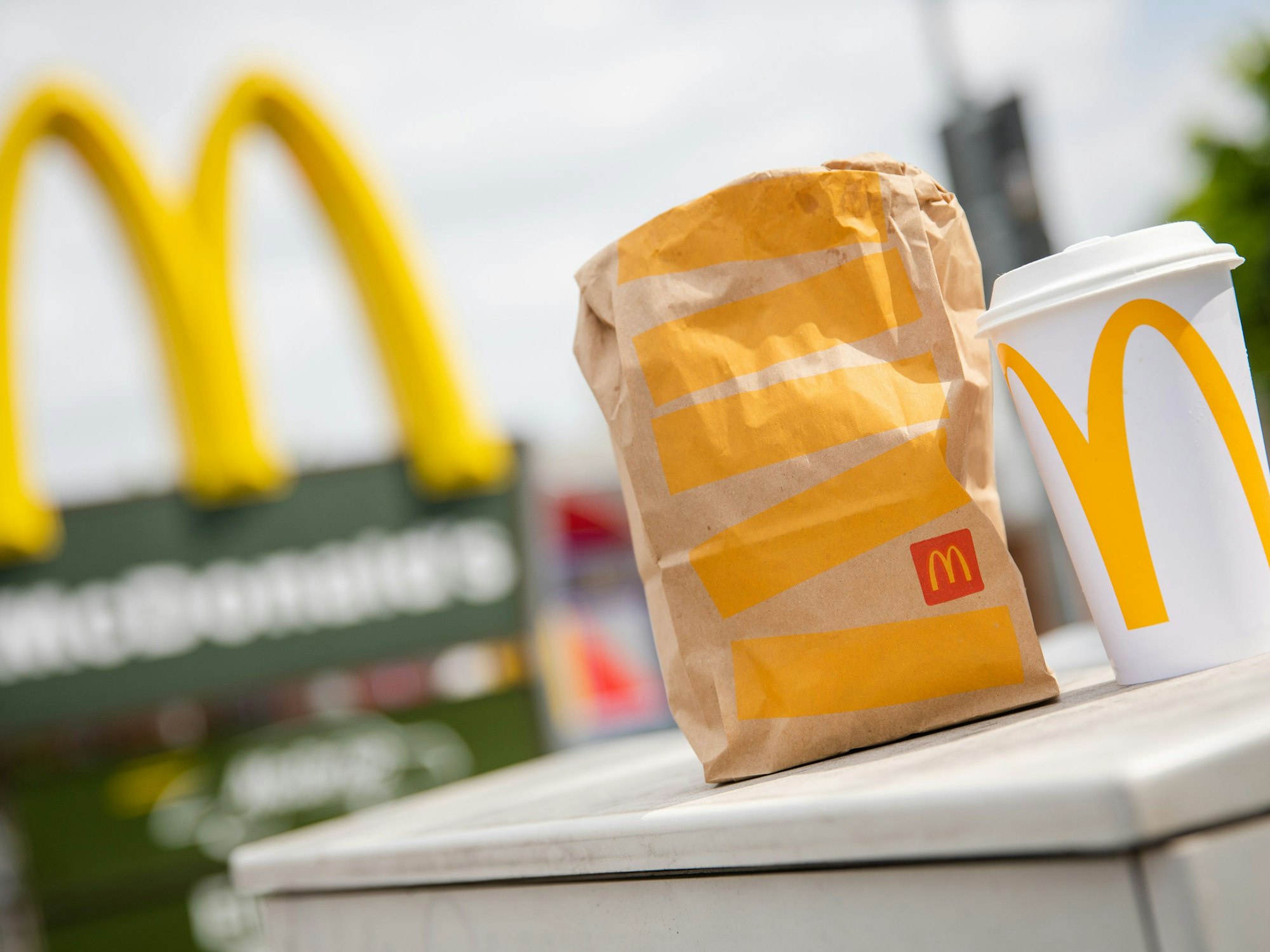 Eine McDonald's To-Go-Tüte und ein To-Go-Becher stehen vor einer McDonald's-Filiale.