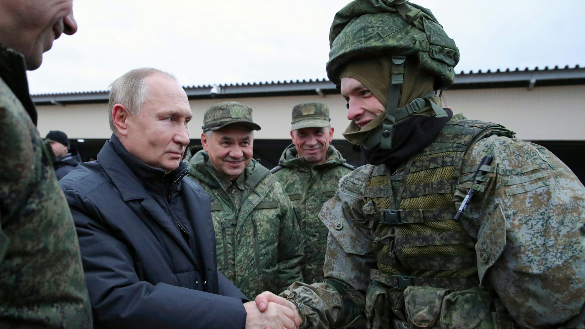 Der russische Präsident Wladimir Putin schüttelt einem Soldaten Mitte Oktober 2022 die Hand, und der russische Verteidigungsminister Sergej Schoigu steht lächelnd neben ihm.