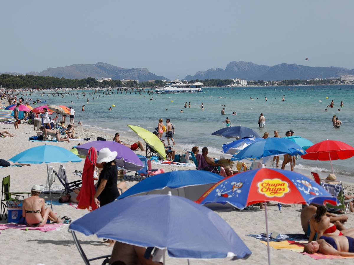 Menschen liegen unter bunten Sonnenschirmen am Playa de Muro.