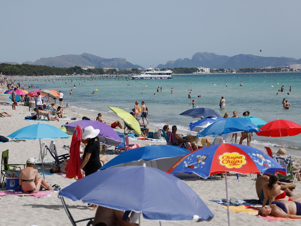 Menschen liegen unter bunten Sonnenschirmen am Playa de Muro.