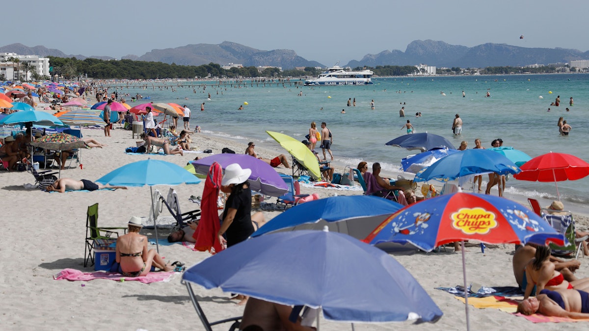 Menschen liegen unter bunten Sonnenschirmen am Playa de Muro.