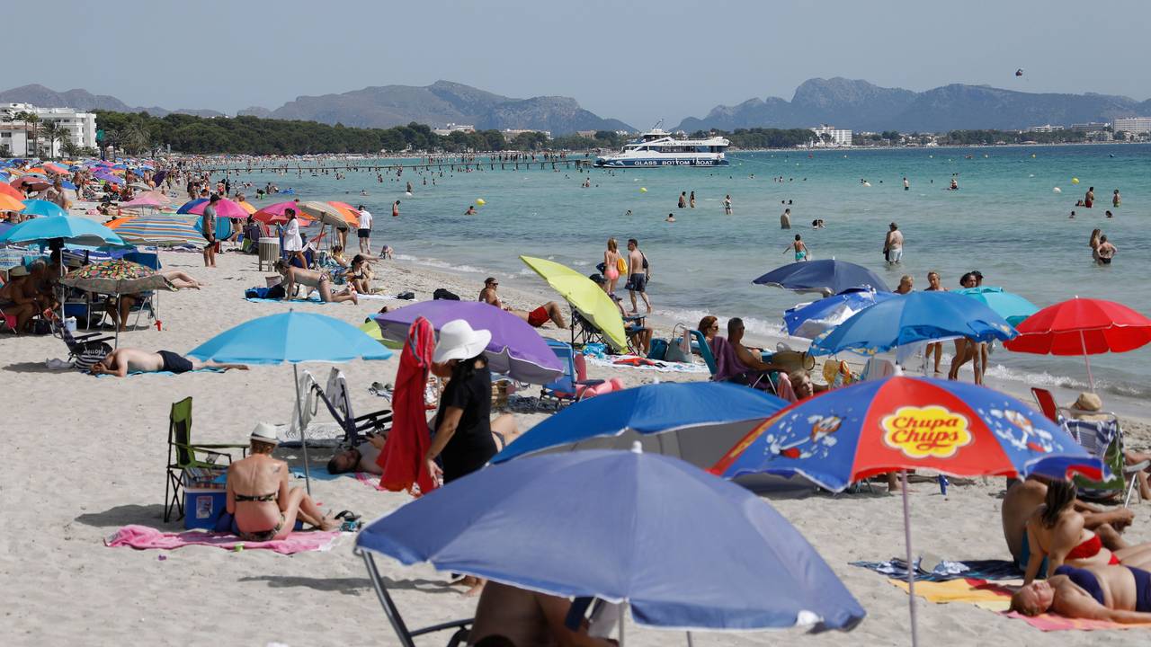 Menschen liegen unter bunten Sonnenschirmen am Playa de Muro.