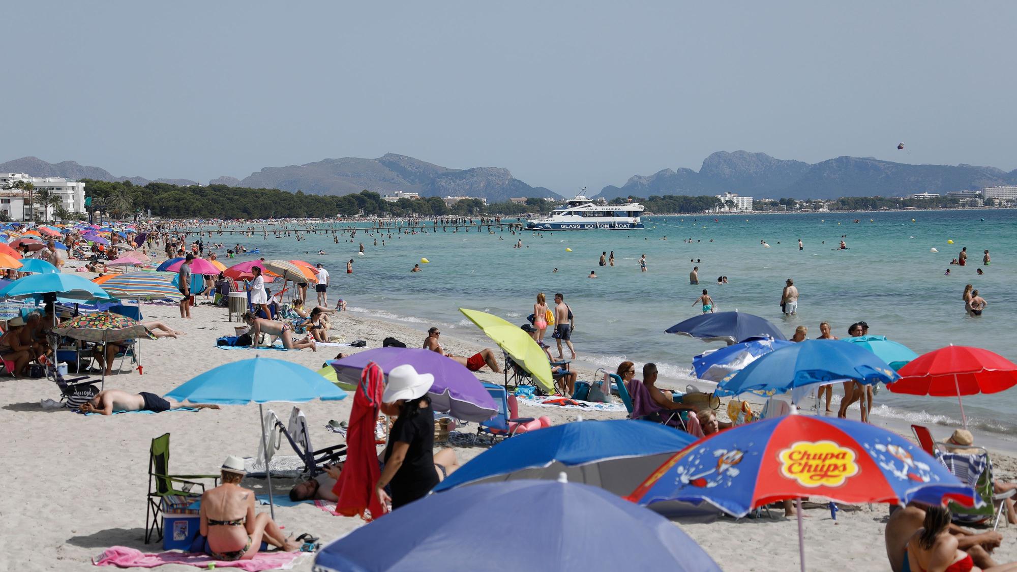 Menschen liegen unter bunten Sonnenschirmen am Playa de Muro.