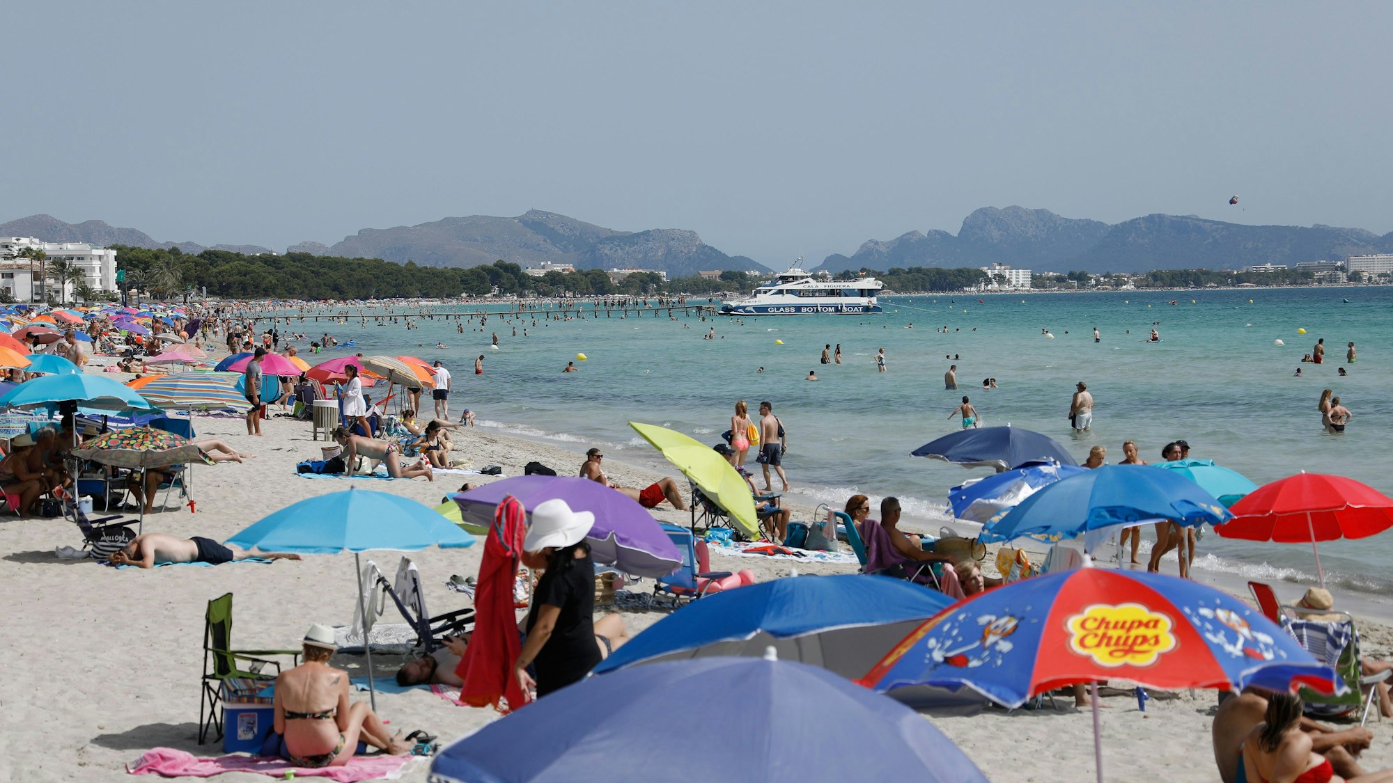 Menschen liegen unter bunten Sonnenschirmen am Playa de Muro.