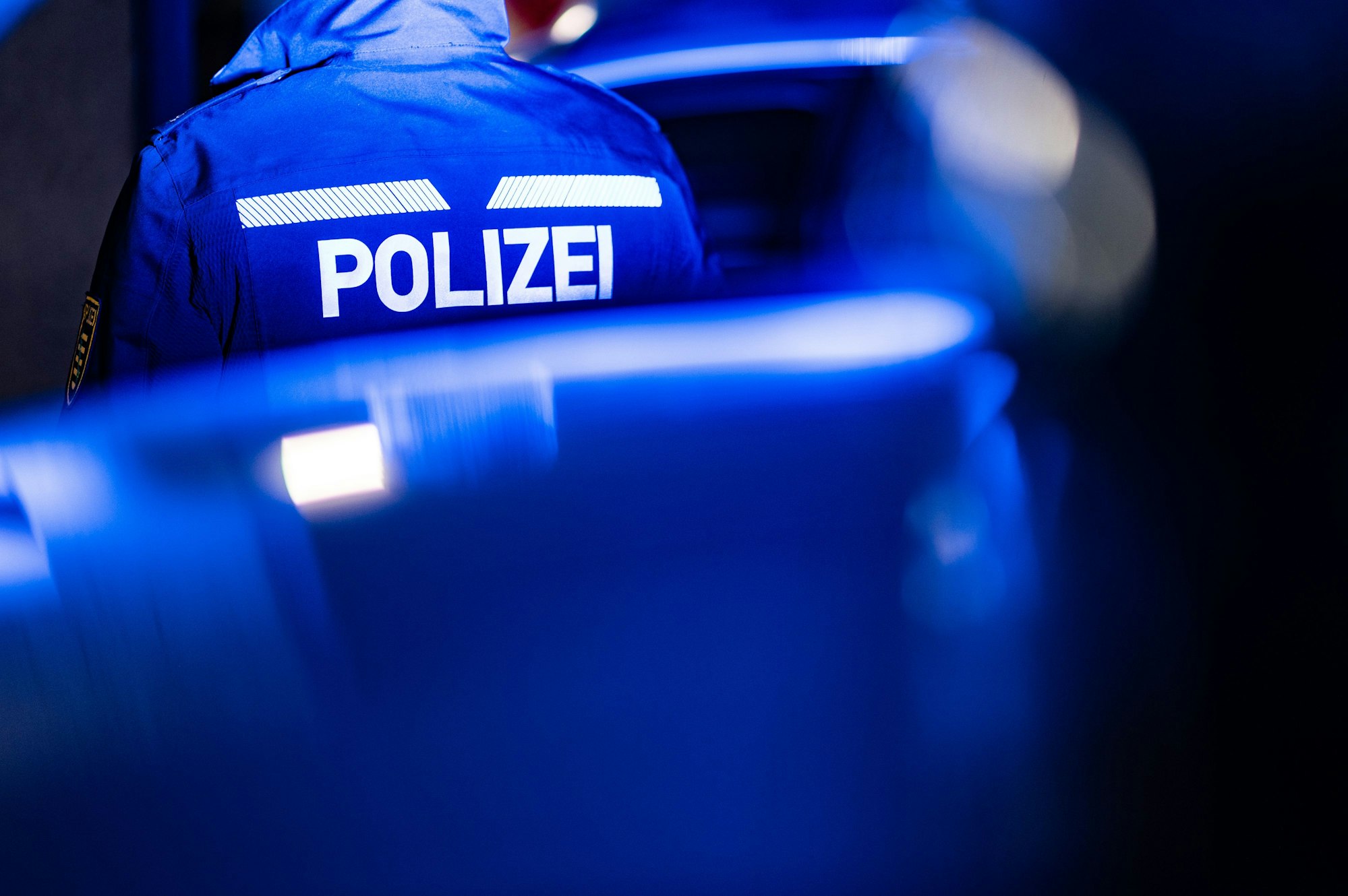 Ein Polizist steht neben einem Streifenwagen.