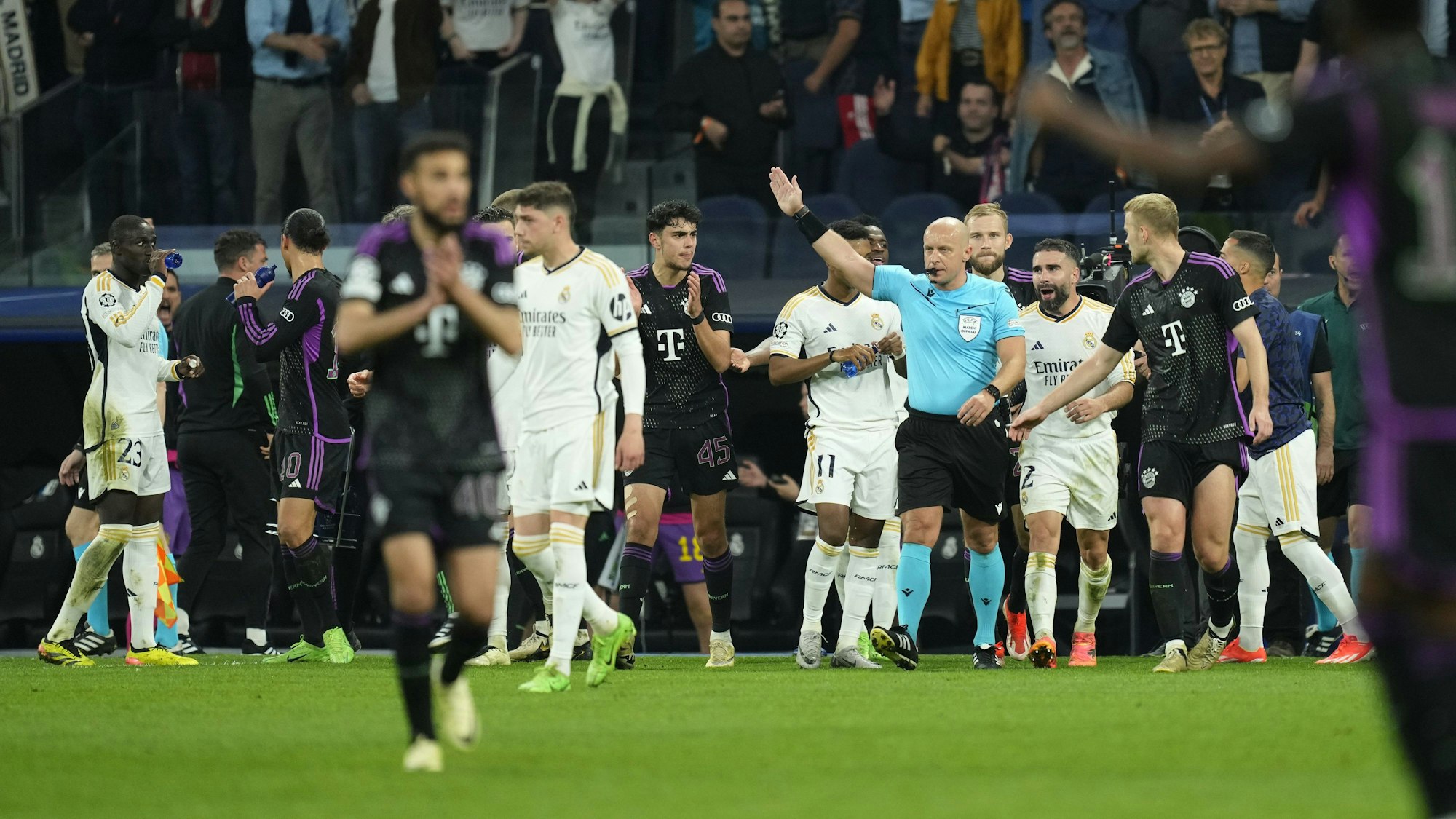 Schiedsrichter Szymon Marciniak greift, belagert von etlichen Spielern von Real Madrid und Bayern München, im Halbfinale der Champions League durch.
