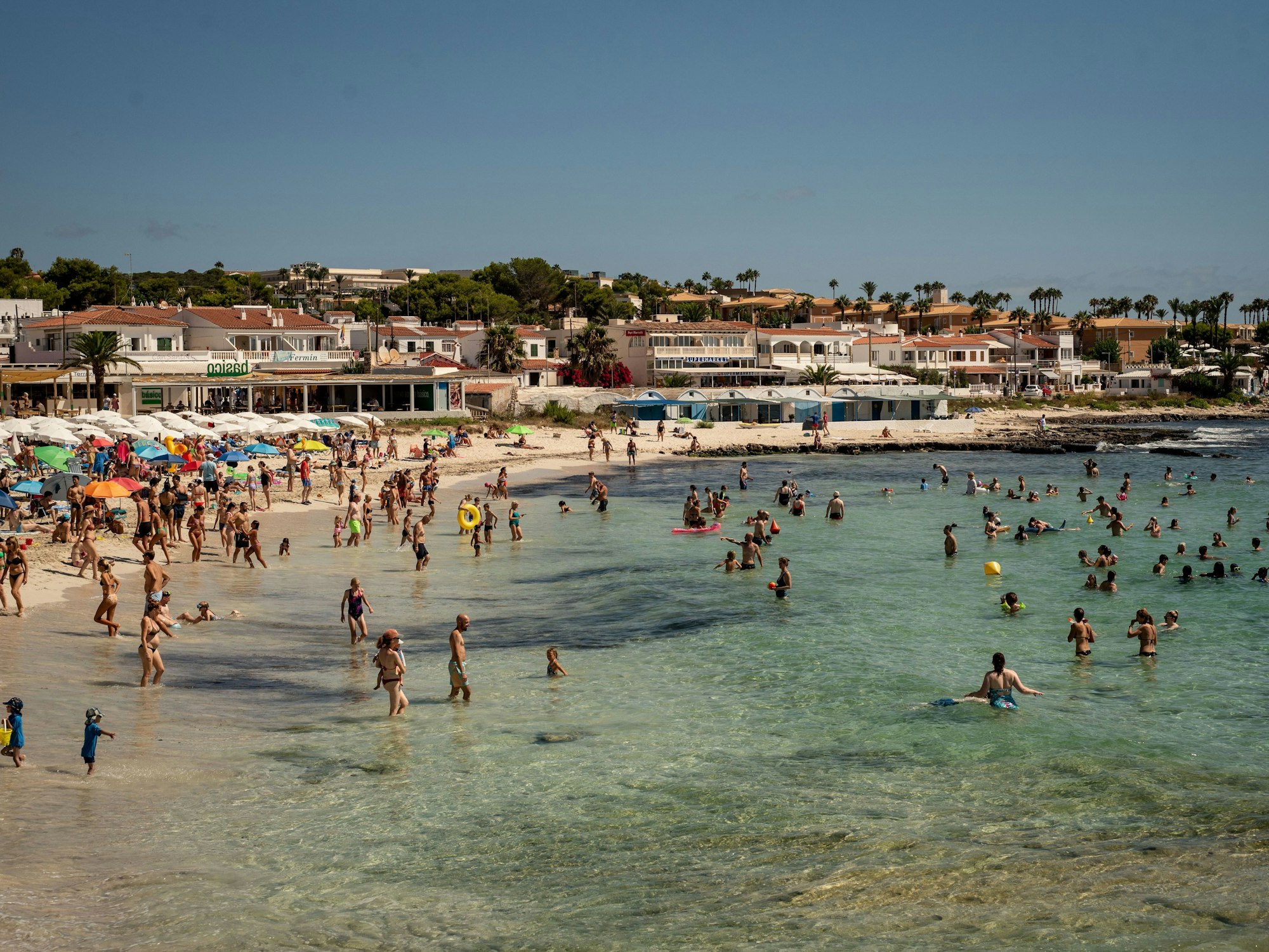 Urlauberinnen und Urlauber kühlen sich am Strand Punta Prima in Sant Lluis im Süden Menorcas im Wasser ab. Das Foto wurde im Sommer 2023 aufgenommen.