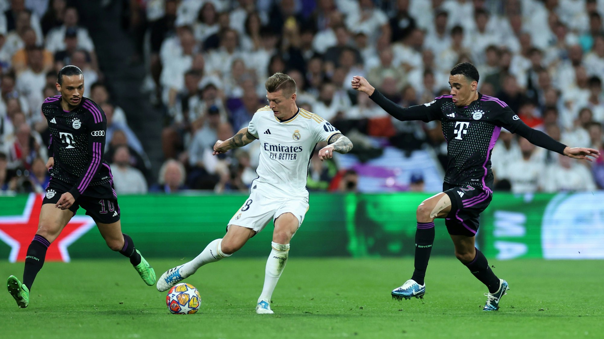 Leroy Sané (l.) und Jamals Musiala (r.) versuchen Reals Toni Kroos den Ball abzunehmen.