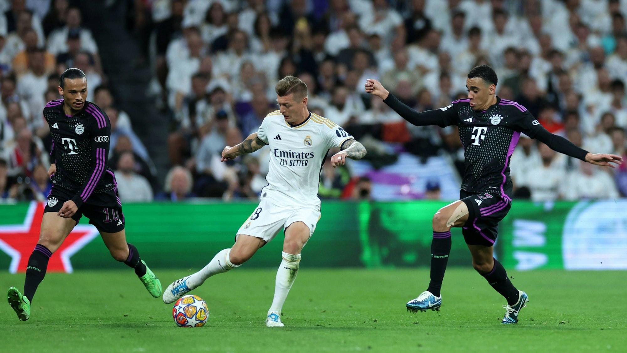 Leroy Sané (l.) und Jamals Musiala (r.) versuchen Reals Toni Kroos den Ball abzunehmen.