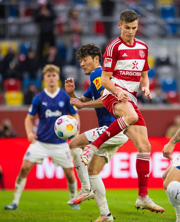 Yannik Engelhardt springt in die Luft und schießt den Ball. Um ihn herum: Spieler von Holstein Kiel.