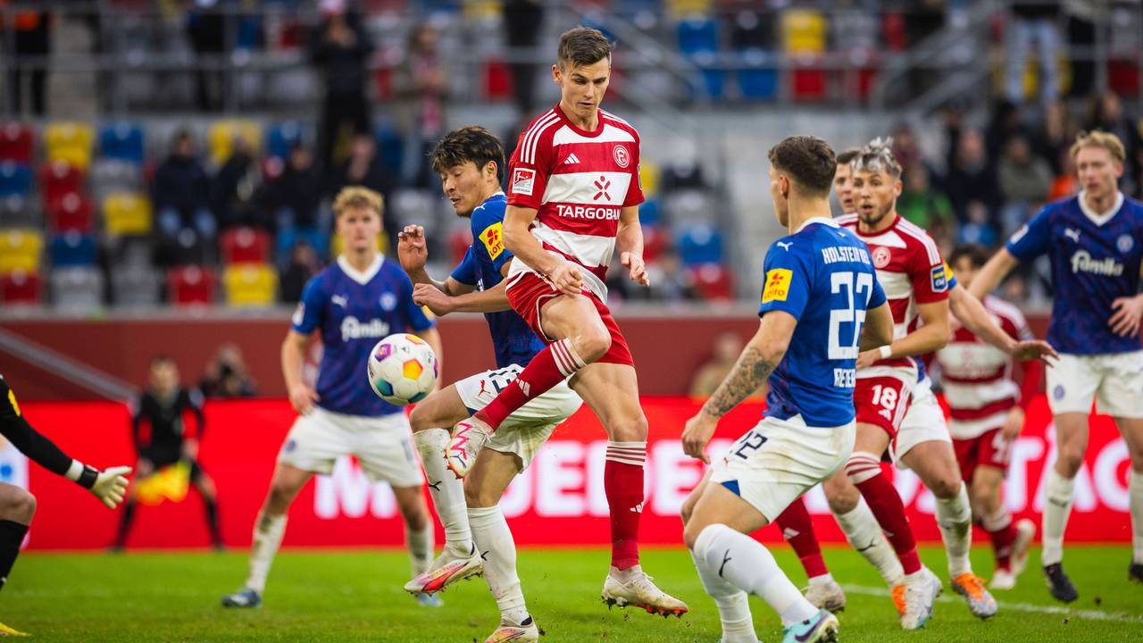 Yannik Engelhardt springt in die Luft und schießt den Ball. Um ihn herum: Spieler von Holstein Kiel.