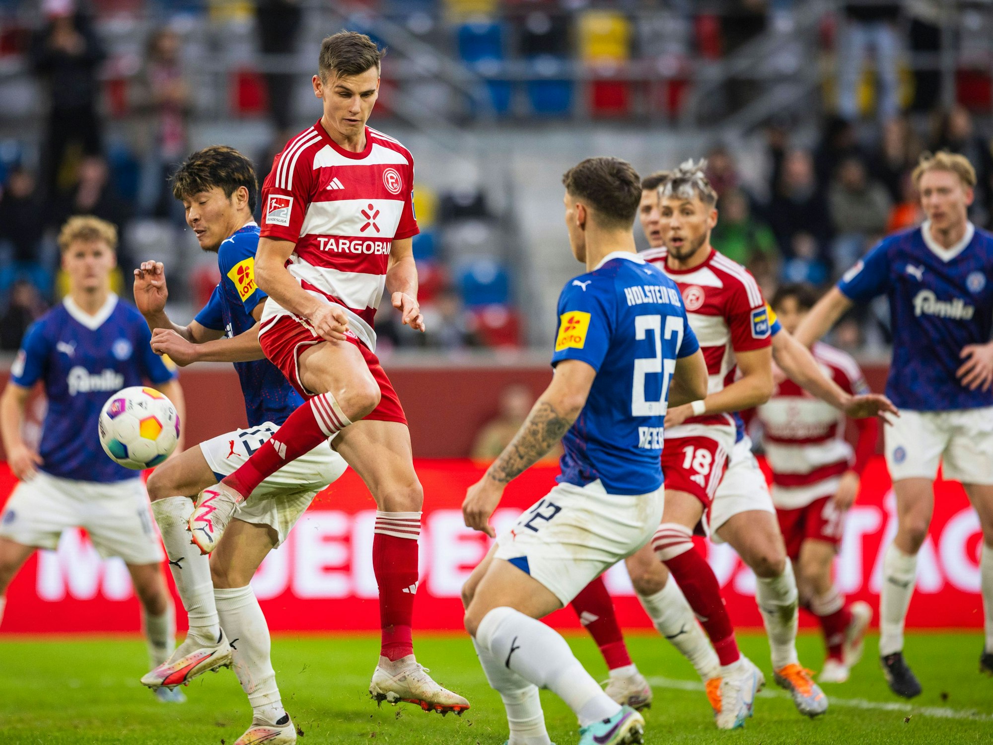Yannik Engelhardt springt in die Luft und schießt den Ball. Um ihn herum: Spieler von Holstein Kiel.