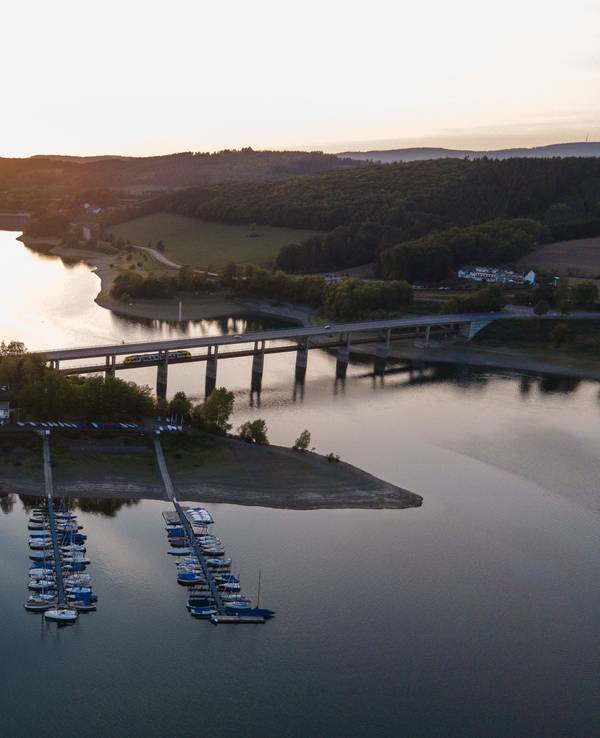 Die Sonne geht am Biggesee hinter einem Segelhafen und einer Brücke unter, hier im September 2020 in Attendorn-Wamge.