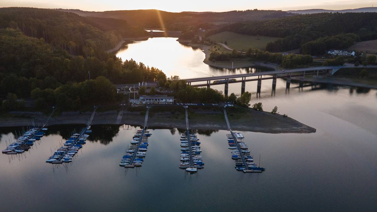 Die Sonne geht am Biggesee hinter einem Segelhafen und einer Brücke unter, hier im September 2020 in Attendorn-Wamge.