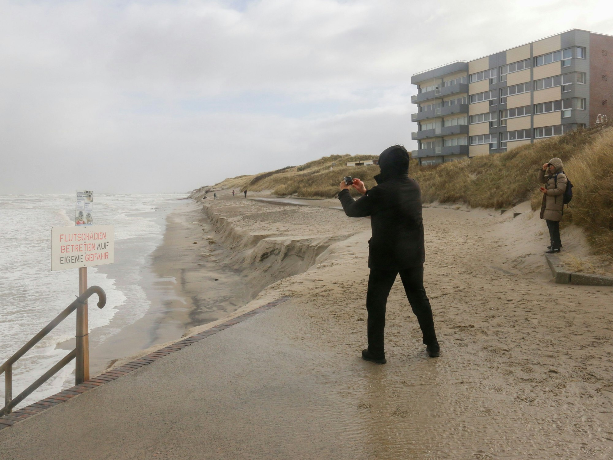 Ein Mann fotografiert 2022 den Strand auf der Insel Wangerooge beim Durchgang eines Sturmtiefs: Ein Junge wurde in einem Sandloch verschüttet, er musste reanimiert werden.