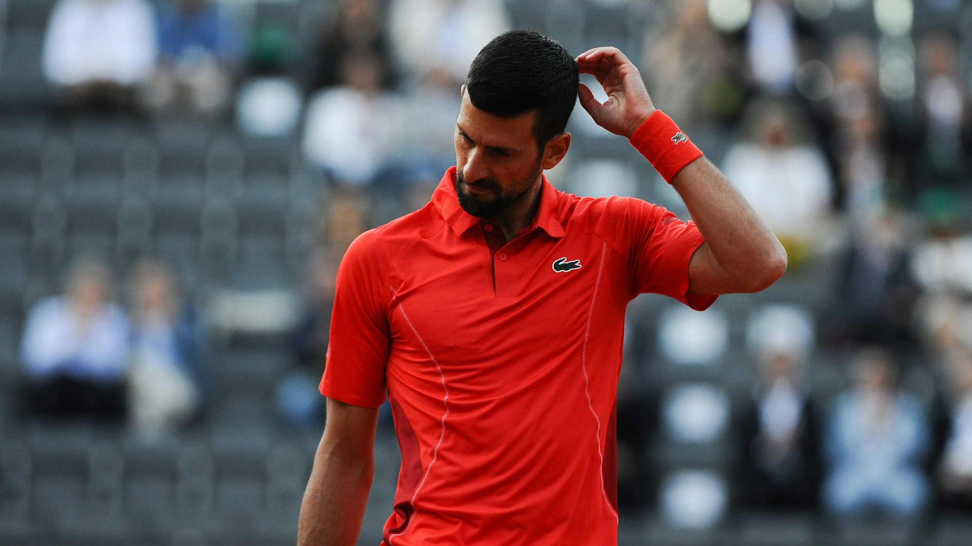 Novak Djokovic kratzt sich auf dem Tennisplatz am Kopf.
