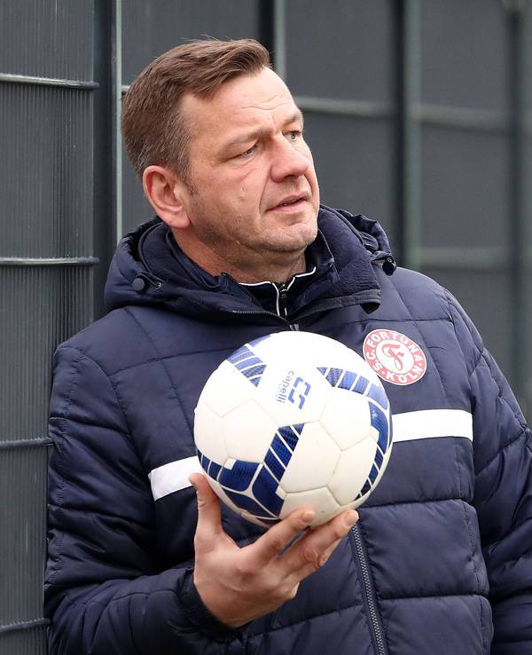 Torwarttrainer Georg Koch lehnt am Zaun und hält einen Ball in der Hand.