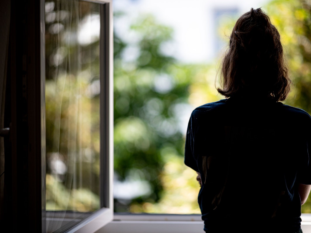 Eine Frau steht in ihrer Wohnung an einem Fenster.