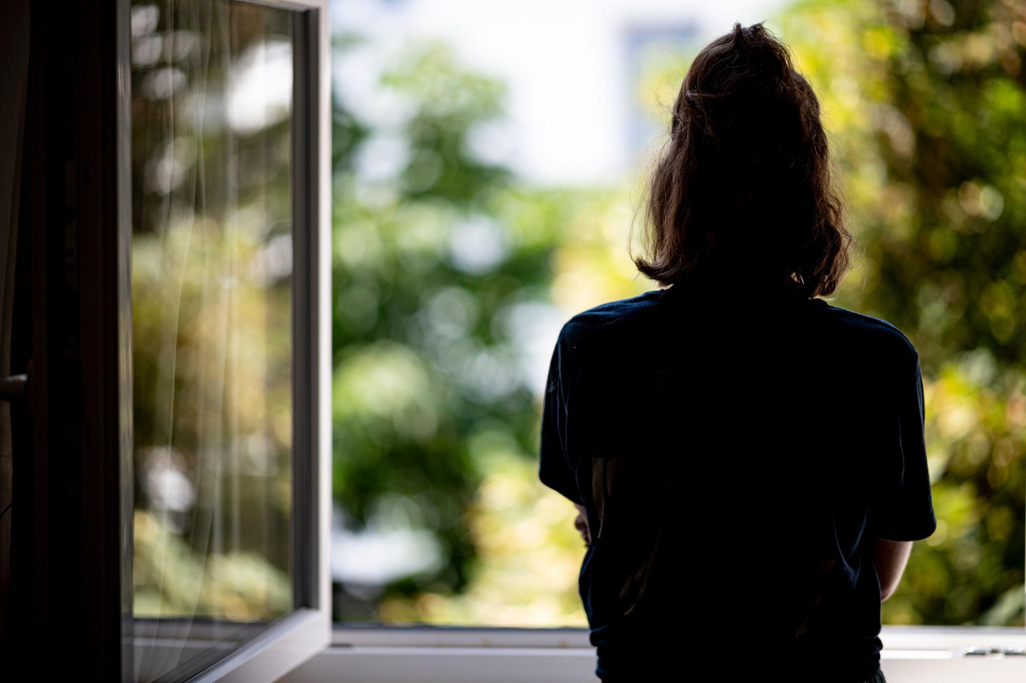 Eine Frau steht in ihrer Wohnung an einem Fenster.
