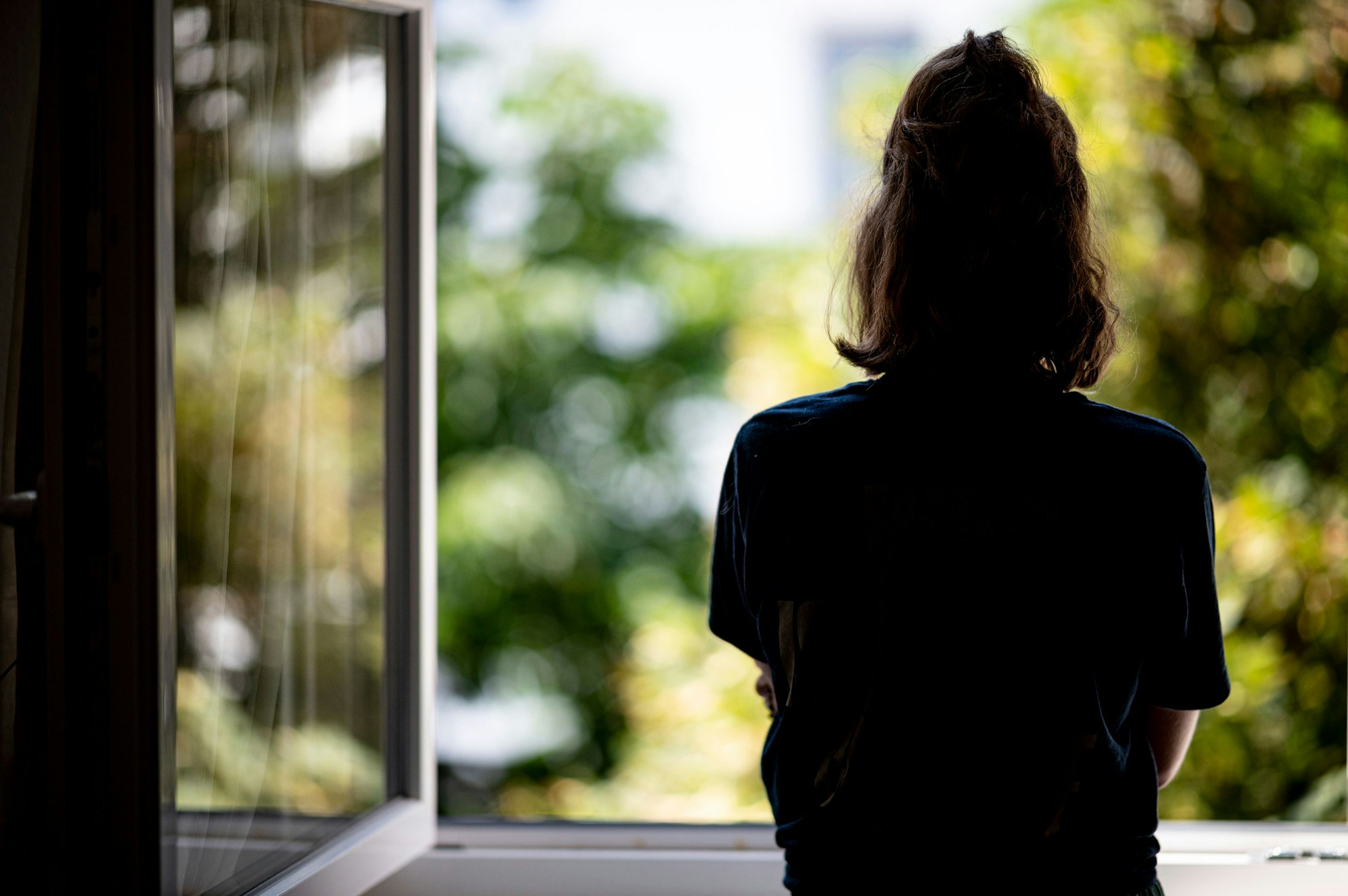 Eine Frau steht in ihrer Wohnung an einem Fenster.