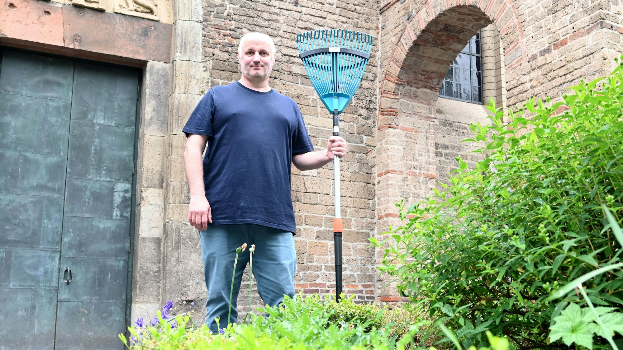 Mitarbeiter Heino Schmidt kümmert sich um die Pflege des Gartens im Schatten des Kirchengemäuers.