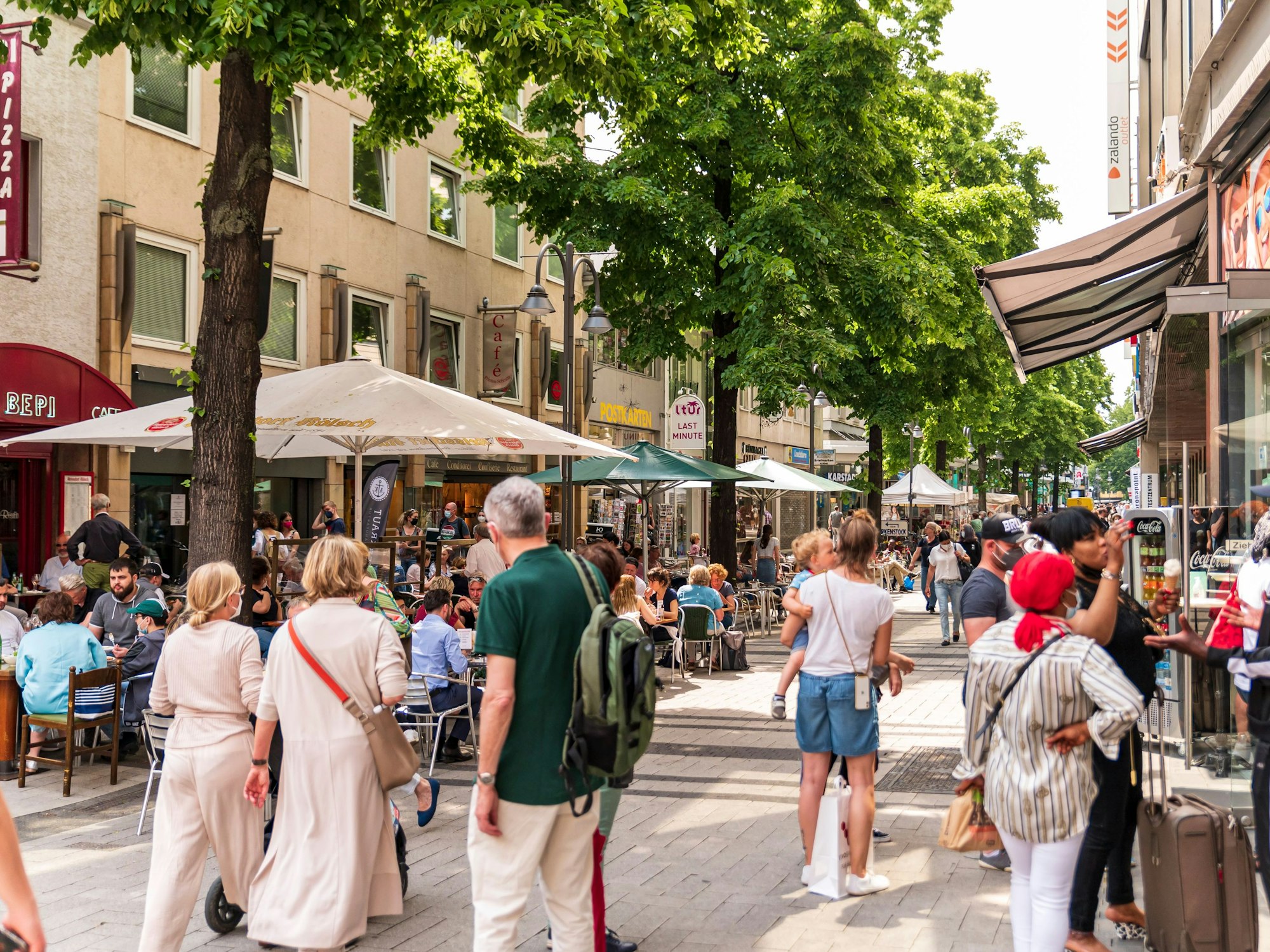 Menschen sitzen in Restaurants oder gehen durch die Breite Straße in Köln.