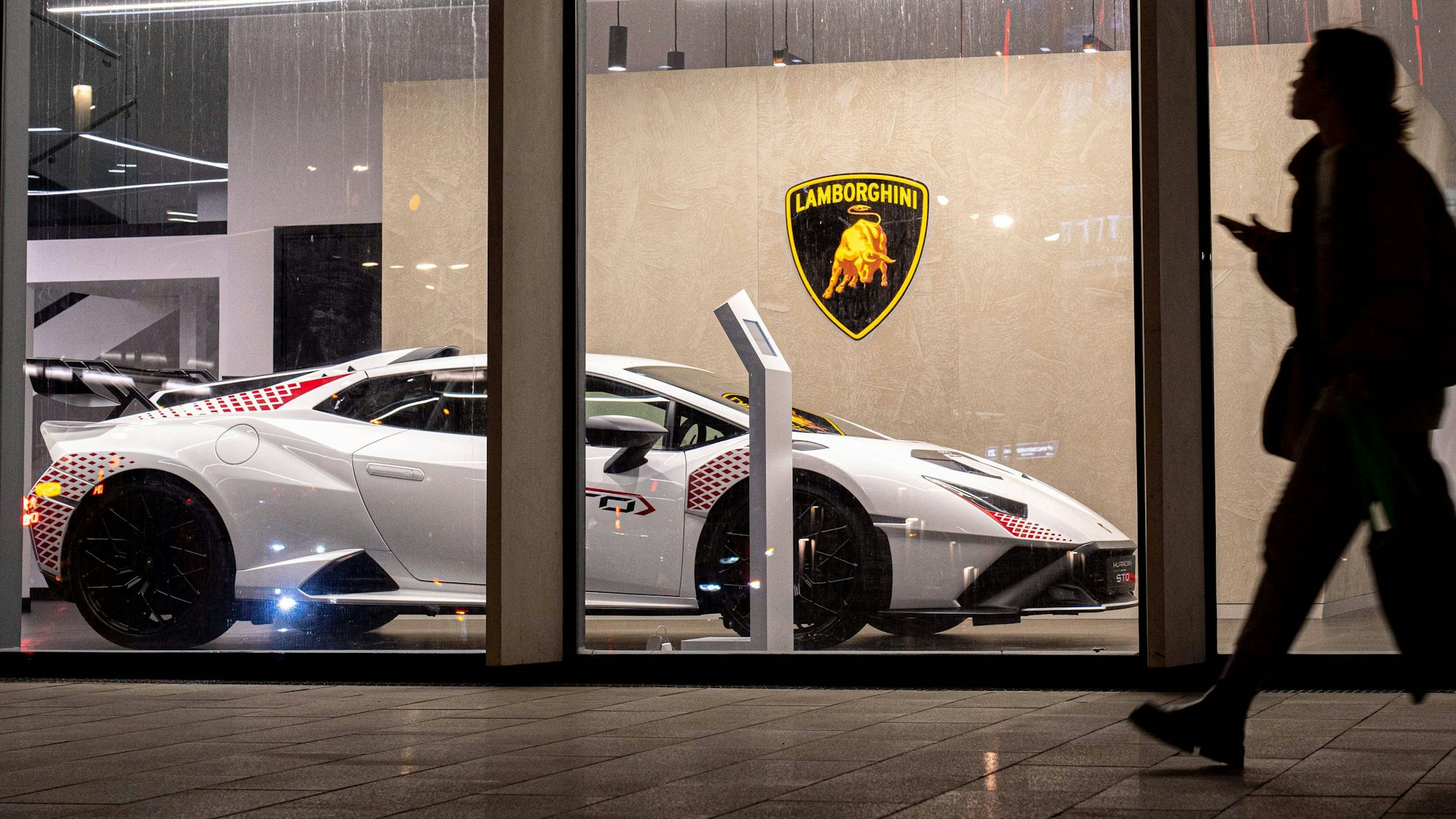 Eine Frau läuft an einem Lamborghini-Autohaus vorbei.