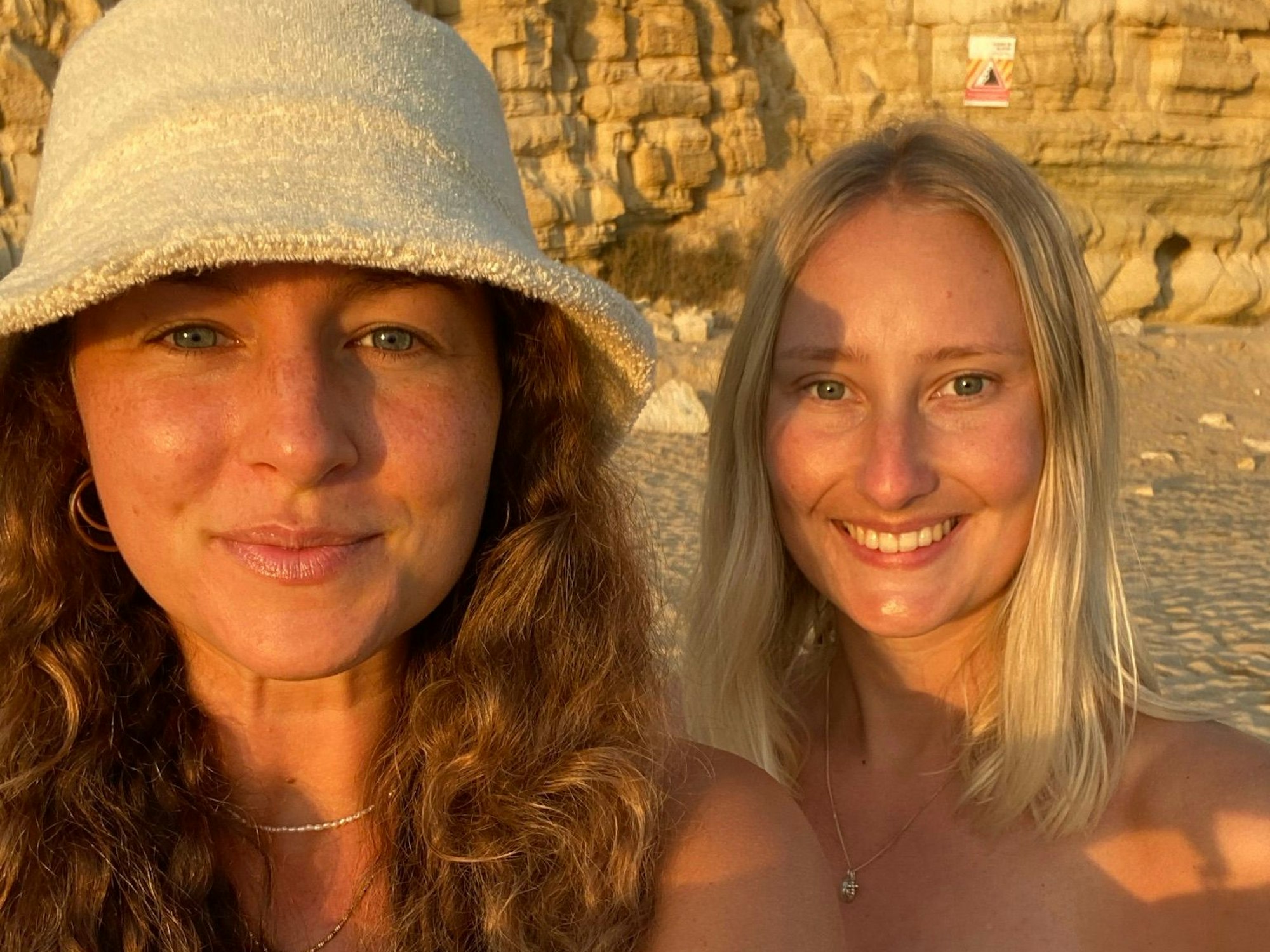 Zwei Frauen machen an einem Strand ein Selfie und grinsen in die Kamera.