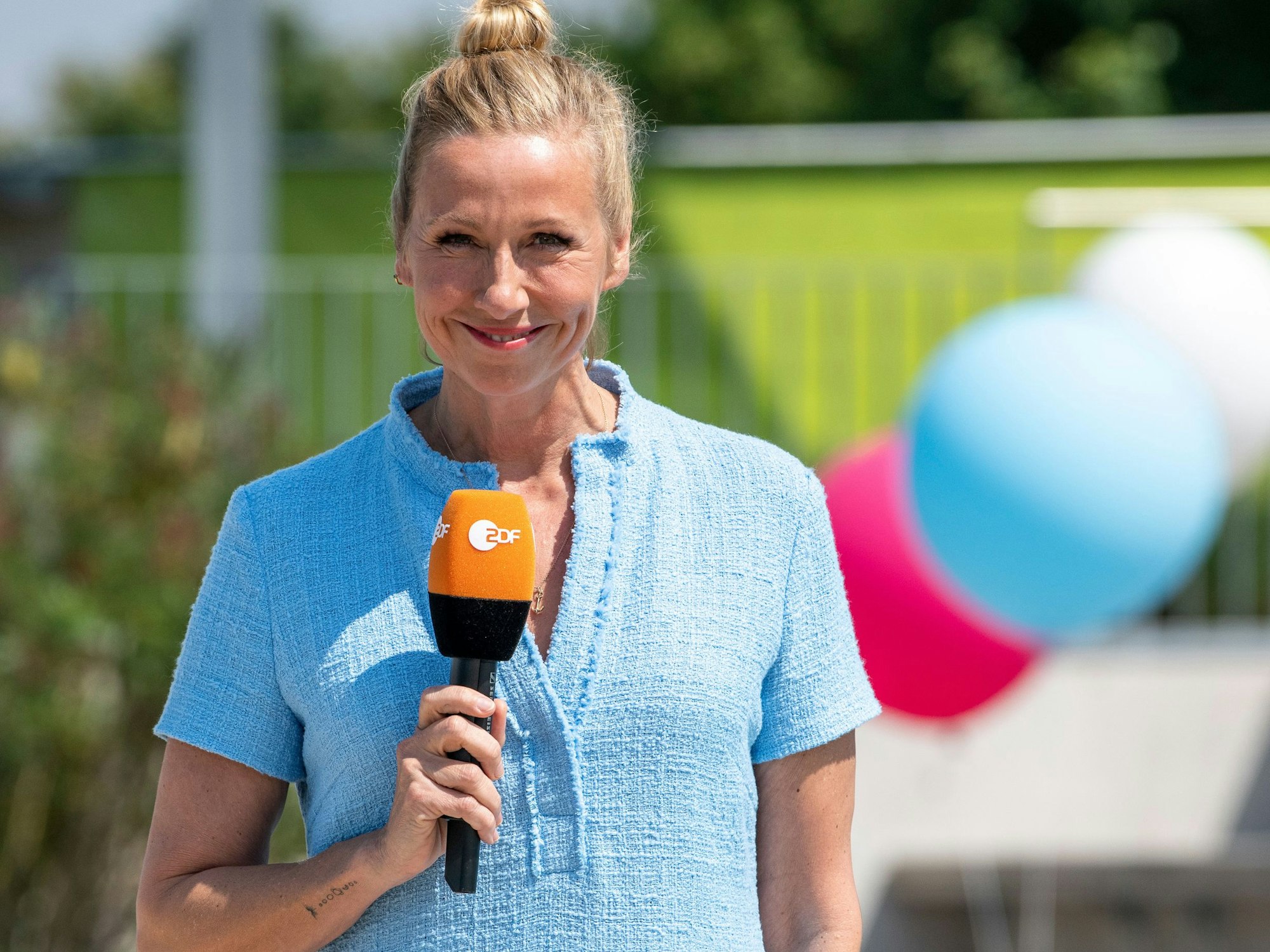 Andrea Kiewel steht im „Fernsehgarten“ und lächelt in die Kamera.