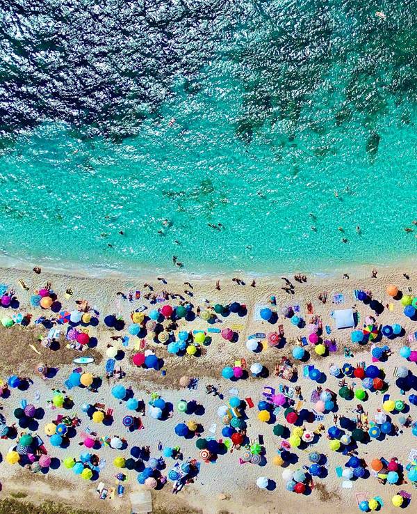 An einem Strand auf Sardinien liegen viele Menschen am Strand.