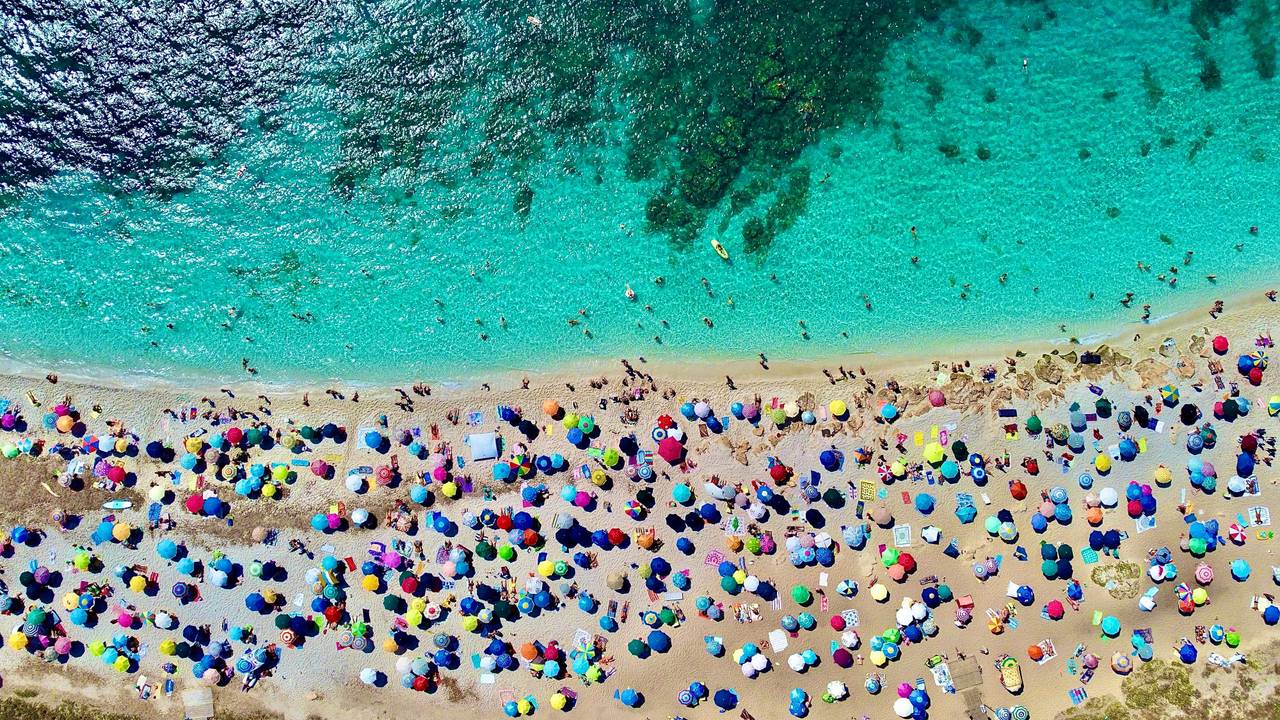 An einem Strand auf Sardinien liegen viele Menschen am Strand.