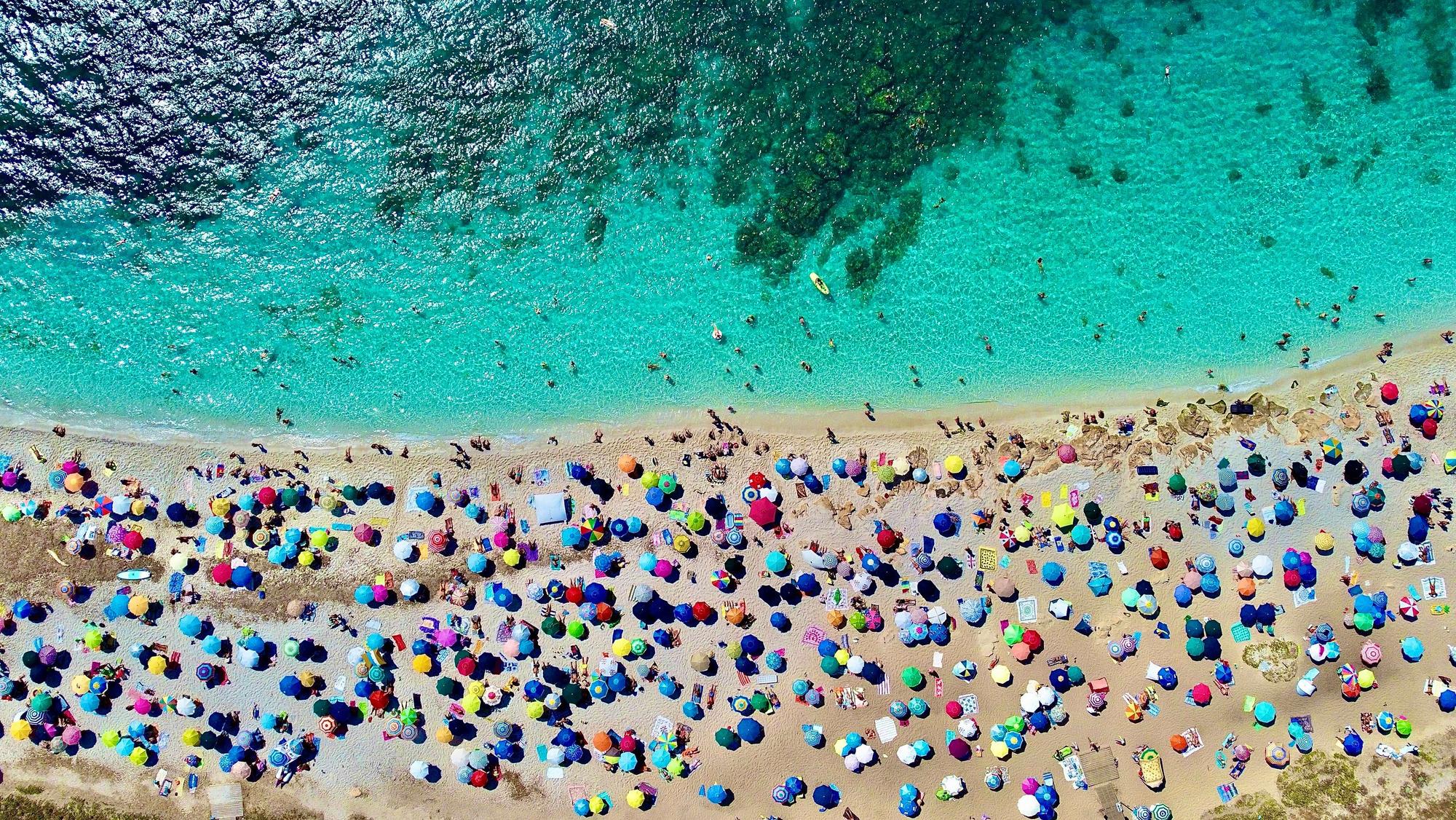 An einem Strand auf Sardinien liegen viele Menschen am Strand.