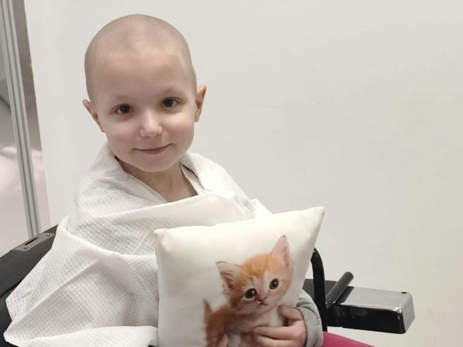 Emily sitzt im Rollstuhl und drückt ein Kissen mit dem Bild einer kleinen Katze an sich.