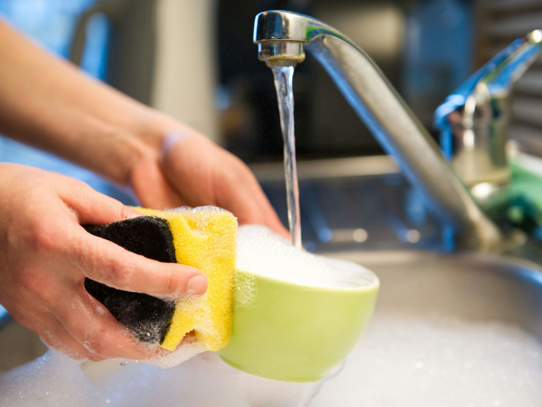 Eine Person spült Geschirr mit einem Putzschwamm im Spülbecken, hier im Oktober 2015 in Berlin.